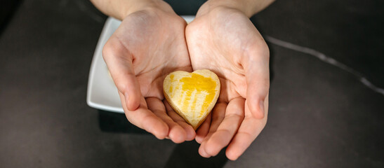 Banner of unrecognizable female pastry chef hands holding a freshly baked heart shaped cookie with egg glaze, showcasing her passion and love for baking
