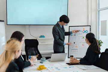 Male presenter explaining financial data to a diverse team in a boardroom.