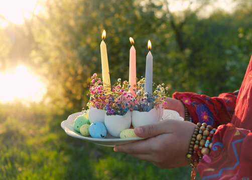 plate with candles and flowers in eggs shells in hands outdoor, natural background. symbol of Easter holiday, Ostara or Nowruz. festive decor for spring season