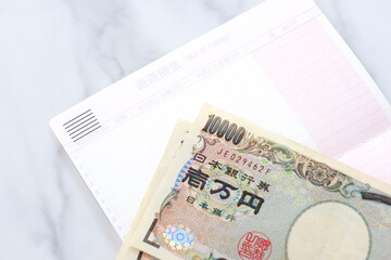 テーブルの上に開いた状態で置かれた銀行の預金通帳と、1万円札
