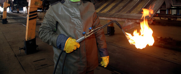 Worker using a flame torch in an industrial workshop during daytime hours to weld metal components