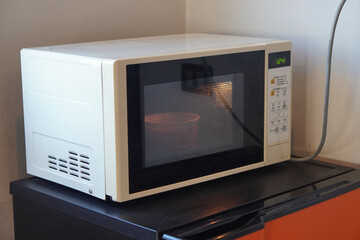 side view white microwave oven placed on an orange and black refrigerator, white wall background,...