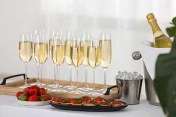 Champagne, ice bucket, strawberries and canapes with red caviar on white table indoors