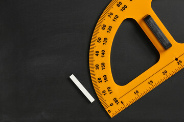 Protractor ruler and chalk on black chalkboard, top view. Space for text
