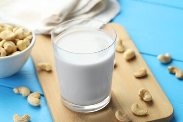 Fresh cashew milk in glass and nuts on light blue wooden table, closeup