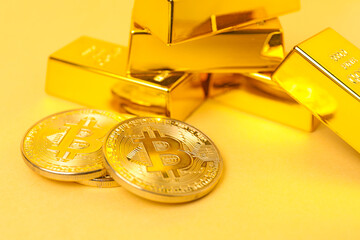 Gold bars and coins on pale yellow background, closeup