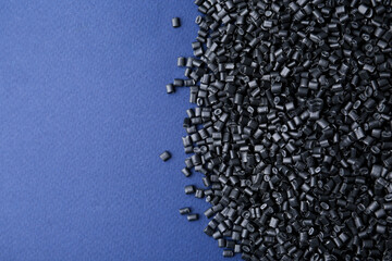 Pile of black plastic granules on blue background, top view. Space for text