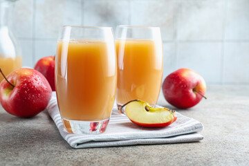 Refreshing apple juice in glasses and fruits on grey textured table, closeup