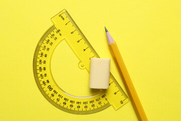Eraser, pencil and protractor on yellow background, top view