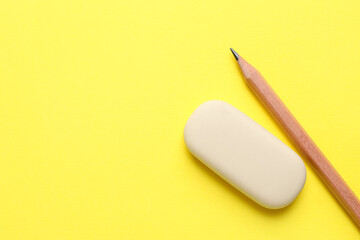 Eraser and pencil on yellow background, top view. Space for text