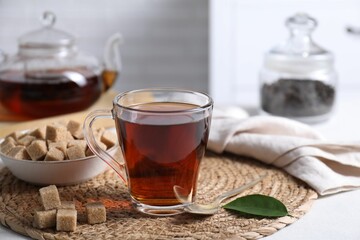 Aromatic black tea in cup and brown sugar cubes on white table, closeup