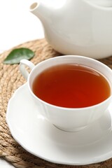 Aromatic black tea in cup and teapot on white table, closeup