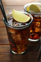 Refreshing iced cola with lemon slices on wooden table, closeup
