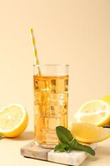 Refreshing iced tea with drinking straw in glass, mint and lemon on beige background, closeup