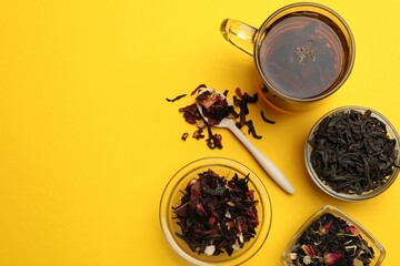 Aromatic tea and dried leaves on yellow background, flat lay. Space for text