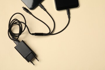Triple charge cable connected to smartphones on beige background, flat lay. Space for text