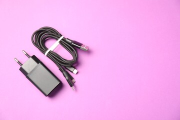USB power adapter and triple charge cable on violet background, flat lay. Space for text