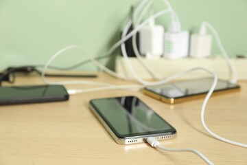 USB adapters with cables plugged into power strip charging devices on wooden table, closeup