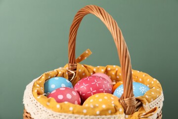 Many decorated Easter eggs in wicker basket on green background, closeup