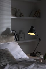 Glowing night lamp and alarm clock on bedside table indoors