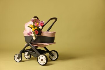 Stylish doll stroller and tulips on olive background, space for text. Kid's toy