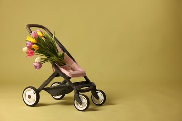 Stylish doll stroller and tulips on olive background, space for text. Kid's toy