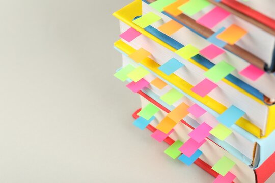 Books with colorful tabs on light gray background, closeup. Space for text