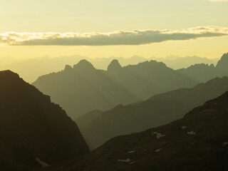 Obraz premium Serene Dolomites at sunset, mountain peaks forming soft layered silhouettes. Warm golden hues fill sky, contrasting misty valleys. Stunning natural scenery attracting hikers, wanderers, landscape love