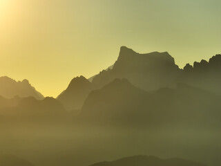 Scenic mountain aerial view sunset, Dolomites bathed in warm golden light. Jagged peaks fade misty background, dreamy composition. Light rays enhance depth, creating natural scenery travel, adventure