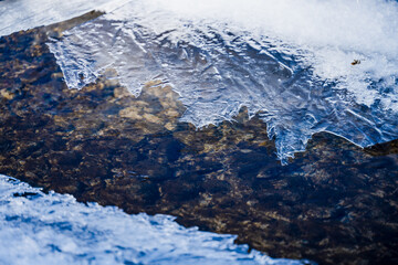 mountain river with pebbles at the bottom covered with ice with patterns