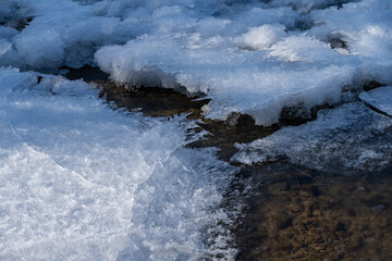 mountain river with pebbles at the bottom covered with ice with patterns