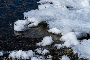 mountain river with pebbles at the bottom covered with ice with patterns