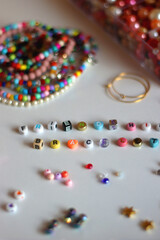 Friendship bracelet spelled with letter beads. Colorful handmade bracelets and various jewelry making supplies. Selective focus, white background.