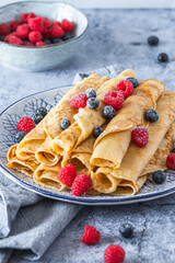 Pile of rolled pancakes with rasperries and blueberries on light blue background
