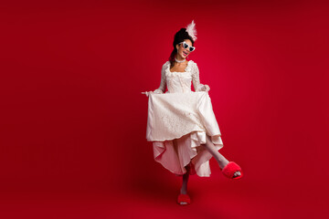 Charming young woman in an elegant white baroque gown and heart-shaped sunglasses on a vibrant red background