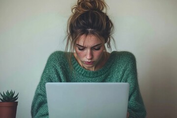 Young woman with messy bun intensely focused on her laptop screen, seemingly engrossed in work or online activity.