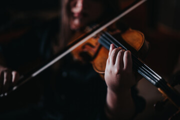 A detailed view of a person's hand playing a violin in a dimly lit setting. The focus captures the...