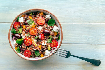 Quinoa salad, healthy Mediterranean lunch with fresh organic vegetables, cheese, and olives, overhead flat lay shot on a wooden background