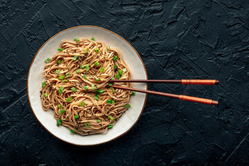 Soba, Japanese buckwheat noodles, boiled, on a plate on a black slate background, with chopsticks, a flat lay