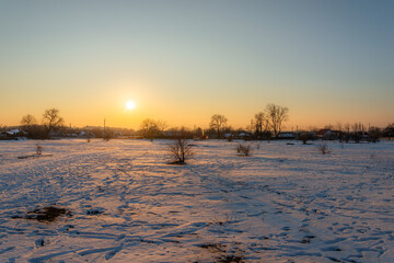 Sunset over the field in the town at winter. Sunny evening,winter landscape. Snow on the groud,beautiful landscape in the town . Orange and blue colors. 