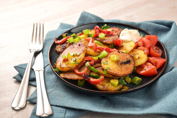 Fried vegetables, potato slices, red bell pepper and green spring onions in a plate on a turquoise napkin, homemade vegetarian meal, selected focus
