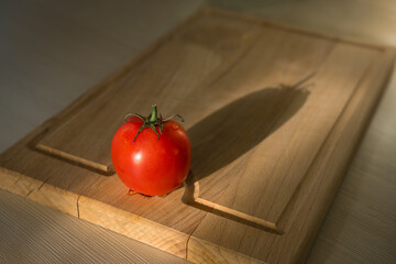 One fresh ripe red tomato on kitchen wooden cutting board. Food background. Light and shadow