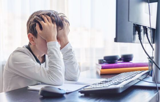 Frustrated student boy 7-9 years old holds head in hands while studying on computer - Concentration problems, digital overload and learning difficulties - Topic ADHD, autism and cognitive problems.  - Powered by Adobe