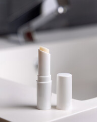 Lip balm stick with blank lid on basin in dark grey modern bathroom close up, cosmetic mockup