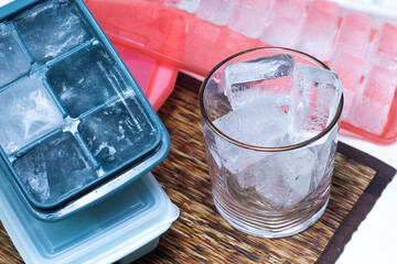 Ice in a clear glass overflows. Next to it is a plastic ice block