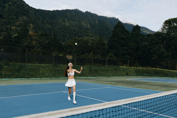 Obraz premium Female tennis player in white sportswear serving on outdoor blue court surrounded by greenery, showcasing determination and focus