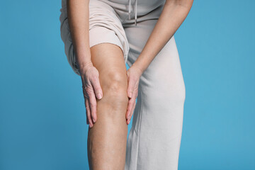 Woman suffering from pain in her knee on light blue background, closeup