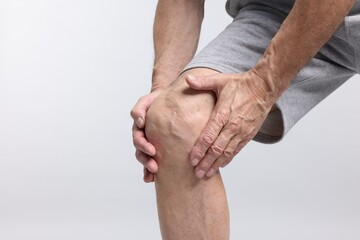 Senior man suffering from knee pain on light grey background, closeup