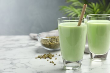 Fresh mung bean juice in glasses and seeds on white marble table, closeup. Space for text