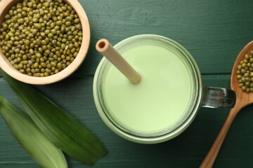 Fresh mung bean juice in mason jar, seeds and leaves on green wooden table, flat lay